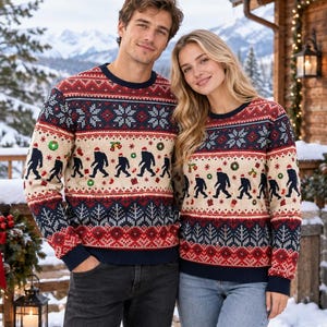 May include: A long-sleeve crew neck sweater featuring a festive holiday pattern with a cream-colored center band displaying silhouettes of Bigfoot figures wearing Santa hats, interspersed with small wreaths, bells, and gifts, framed by navy and red borders.