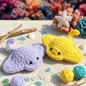 May include: Crocheted sea creatures, including a lavender stingray and a yellow stingray, are displayed with seashells, driftwood, and yarn balls. A crocheted starfish and coral are in the background, creating an underwater theme.
