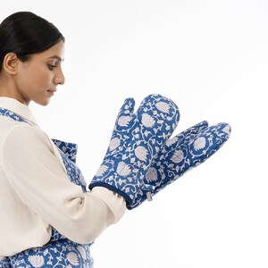 May include: A woman wearing a blue and white floral apron and matching oven mitts. The apron has a white floral pattern on a blue background.