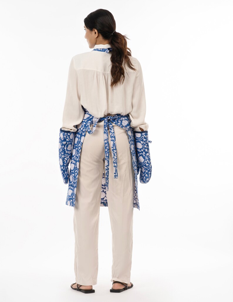 May include: A blue and white floral print apron with long sleeves and two pockets. The apron is tied at the waist with a blue ribbon.
