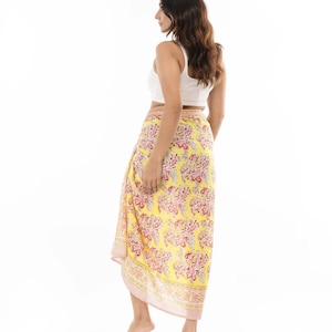 May include: A bright yellow sarong featuring a repeating floral pattern in shades of red and white. The fabric is wrapped around the waist, extending to the lower calf, and is finished with a striped border along the bottom edge and side.