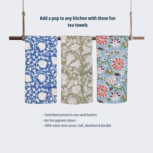 May include: Three hand-printed tea towels hanging on a wooden rod. The towels feature floral patterns in blue, green, and orange on a white background. The text on the image reads: "Add a pop to any kitchen with these fun tea towels - Hand block printed in very small batches - Azo free pigment colours - 100% cotton duck canvas: Soft, absorbent & durable"