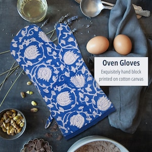 Op de afbeelding: Blauwe ovenwant met een wit bloemenpatroon. De want is gemaakt van katoenen canvas en is met de hand bedrukt. De tekst "Oven Gloves" en "Exquisitely hand block printed on cotton canvas" is zichtbaar in de afbeelding.