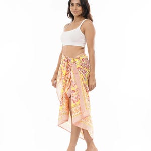 May include: A yellow sarong featuring a vibrant floral pattern in shades of pink, orange, and white. The fabric is tied at the waist, creating a draped silhouette with a side slit. The design includes a striped border detail along the edges.