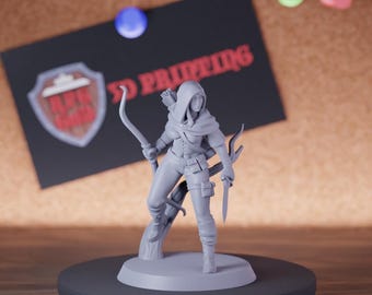 May include: A gray 3D-printed figurine of a hooded archer with a bow and arrow, standing on a circular base. The figure is holding a knife and is posed as if ready for action. A black card with red text and a logo is in the background.