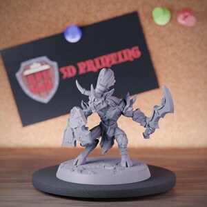 Puede incluir: Una figura miniatura gris sin pintar de una criatura con cuernos y una amplia sonrisa, que sostiene un escudo dentado en una mano y una hoja curva en la otra. La figura se apoya sobre una base circular con una superficie texturizada.