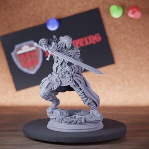 Könnte beinhalten: Graue Miniaturfigur eines Kriegers in dynamischer Pose, der ein Schwert hält. Die Figur ist detailliert mit Rüstung und Kleidung, die auf einem felsigen Sockel steht. Eine schwarze Karte mit rotem Text und einem Schildlogo befindet sich im Hintergrund.
