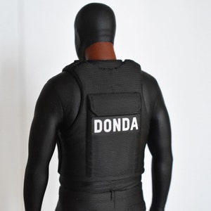 May include: A black figure wearing a black balaclava and a black vest with the word "DONDA" printed in white on the front.