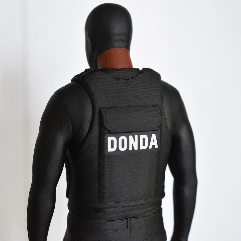 May include: A black figure wearing a black balaclava and a black vest with the word "DONDA" printed in white on the front.