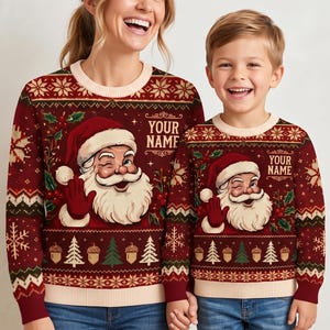May include: Two matching dark red long-sleeve jumpers featuring a graphic of a winking Santa Claus, holly berries, and pine trees. The jumpers include a cream-coloured crew neckline and cuffs, with the text YOUR NAME printed on the front.