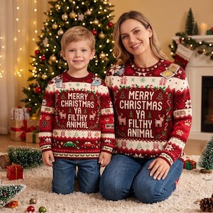 May include: Two long-sleeve knit jumpers featuring a deep red base with white and green holiday patterns. The text MERRY CHRISTMAS YA FILTHY ANIMAL is centred on the chest, surrounded by reindeer, cars, and gift icons in a festive knit design.