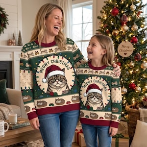 May include: Two matching long-sleeve jumpers in dark green, cream, and maroon. The jumpers feature a central graphic of a grumpy cat wearing a Santa hat with the text MEOWY CHRISTMAS, surrounded by smaller cat illustrations and holiday lights.