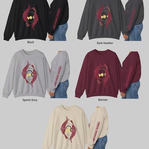 May include: Five different colour options for a sweatshirt with a graphic design of red and gold winged headphones inside a diamond shape with the text "Fierce Wings" on the sleeve. The colours are black, dark heather, sports grey, maroon, and sand.