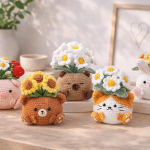 May include: A collection of handmade crochet animal planters, including a pig, bear, cat, bunny, and bear. Each planter is adorned with colorful crochet flowers, such as daisies, sunflowers, and mixed blooms. The planters are displayed on a wooden surface.