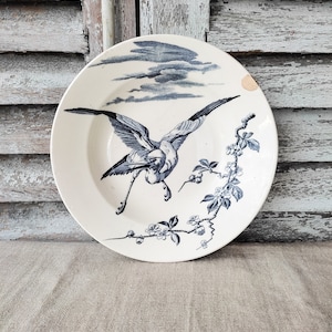 Könnte beinhalten: Ein weißer Keramikteller mit einem blauen und weißen Design eines Vogels im Flug mit einem Zweig mit Blumen und Beeren. Der Teller hat einen abgebrochenen Rand.