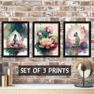 May include: Set of three framed watercolor prints featuring lotus flowers and a woman meditating. The prints have black frames and are displayed on a brick wall.