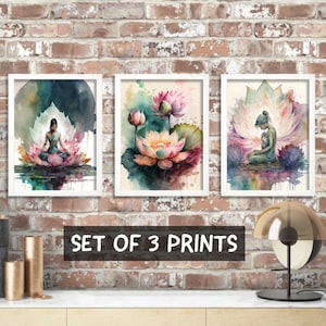 May include: Set of three watercolor prints featuring a woman meditating on a lotus flower, a single lotus flower, and a woman meditating inside a lotus flower. The prints are framed in white and have a watercolor background.