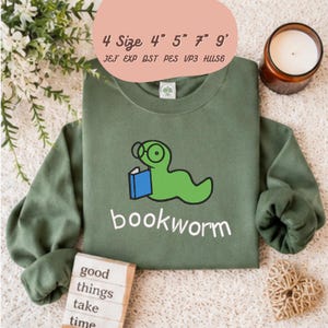 Può includere: Una felpa a maniche lunghe color verde oliva con il ricamo di un verme verde che indossa occhiali tondi e legge un libro blu. Sotto la grafica, la parola bookworm è stampata in bianco. Il testo sopra riporta 4 Size 4" 5" 7" 9" JEF EXP DST PES VP3 HUS6.