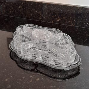May include: A clear glass serving dish set with a decorative, scalloped edge. The set includes a tray and several compartments for serving snacks or appetizers. The glass has a detailed, etched pattern.