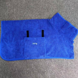 Op de afbeelding: Een blauwe microvezel handdoek met een capuchon en een zak. De handdoek heeft twee zwarte banden op de zak. De handdoek heeft het woord "SnugglePug" op de zak gedrukt.