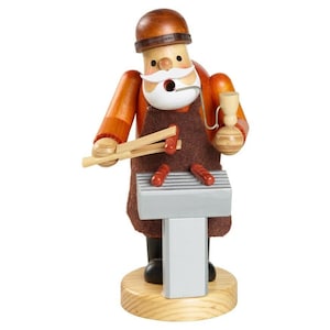 Könnte beinhalten: Eine Räuchermann-Figur aus Holz, die eine Person mit weißem Schnurrbart und braunem Hut darstellt, bekleidet mit einer braunen Schürze über einem orangefarbenen Hemd. Die Figur hält eine Holzzange und eine Pfeife vor einem silbernen Grill mit Würstchen.