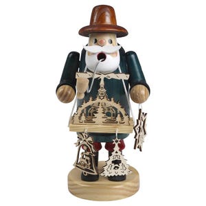May include: A wooden figurine of a man wearing a green jacket and brown hat, holding a wooden tray with a Christmas village scene and ornaments.