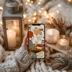 Puede incluir: Un smartphone muestra una ilustración acogedora con una figura pelirroja haciendo mermelada, con el texto "Making jam instead of making decisions". El teléfono se sostiene cerca de una vela encendida, una linterna y una manta suave.