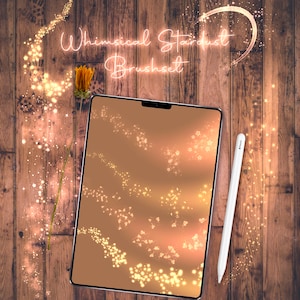 May include: A digital tablet displaying a set of whimsical stardust brushes. The brushes are displayed on a light brown background with a subtle gradient. The tablet is on a wooden surface with a dried flower stem and a white stylus.