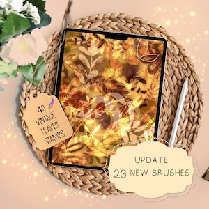 May include: A digital tablet displaying a pattern of gold and brown leaves. The tablet is on a woven straw mat. A tag with the text "40 Vintage Leaves Stamps" is visible. A white stylus is lying on the mat. A text box with the text "UPDATE 23 NEW BRUSHES" is in the foreground.