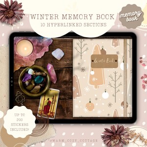 May include: A digital tablet displaying a winter-themed memory book with a beige background and a pattern of white snowflakes, brown trees, and beige ornaments. The text "Winter Book" is written on a brown label. The tablet is on a wooden surface with a bowl of crystals and a lit candle.