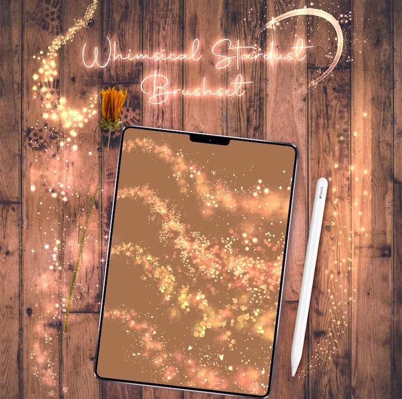 May include: A digital tablet displaying a preview of a whimsical stardust brush set. The tablet is on a wooden surface with a dried flower stem and a white stylus.