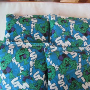 May include: Four blue bean bags with a repeating pattern of the Hulk character, the word "SMASH", and exclamation points. The Hulk is green with purple pants. The bean bags are arranged in a square.