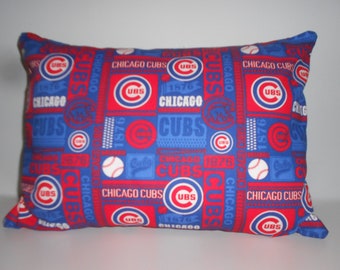 Puede incluir: Una almohada azul y roja con un patrón de los Chicago Cubs. La almohada está cubierta de varios logotipos, incluido el logotipo de los Chicago Cubs, la mascota del equipo y los años 1876, 1972 y 1984.