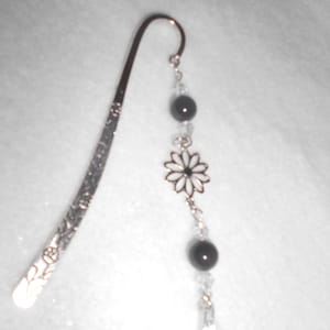 May include: Silver bookmark with a floral design and black beads. The bookmark has a silver loop at the top and a dangling charm with a flower design.