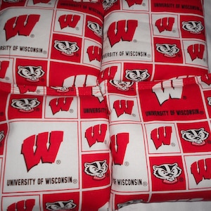 May include: Four red and white bean bags with the University of Wisconsin logo and a badger mascot. The bags are made of fabric and have a sewn seam.