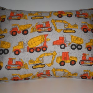 May include: A rectangular pillow with a light gray background and a repeating pattern of construction vehicles. The vehicles are in shades of yellow, orange, and red, with black details. The pillow is a standard size.