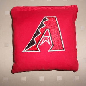 May include: Red bean bag with an embroidered Arizona Diamondbacks logo. The logo is a white outlined red "A" with a black and white star inside.