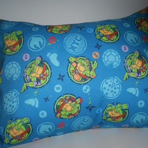 May include: Blue pillowcase with a repeating pattern of Teenage Mutant Ninja Turtles characters, pizza slices, and ninja stars. The background is blue with white accents.