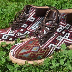 May include: A pair of brown leather ankle boots with a colorful geometric pattern on the fabric. The boots have a lace-up closure and a thick sole.