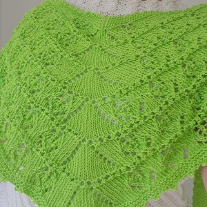 Könnte beinhalten: Ein hellgrüner, gestrickter Schal mit einem geometrischen Muster. Der Schal ist über den Schultern drapiert und zeigt das komplizierte Lochmuster-Design. Die leuchtende Farbe und der strukturierte Strick erzeugen ein optisch ansprechendes Accessoire.