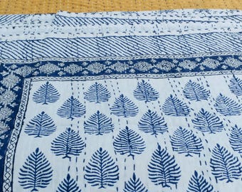 Könnte beinhalten: Eine weiße Baumwolldecke mit einem blauen und weißen Muster. Die Decke hat einen Rand aus blauen und weißen geometrischen Formen und ein zentrales Muster aus blauen Blättern.