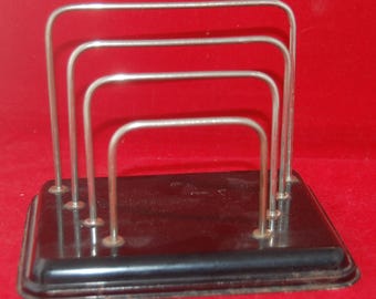 Peut inclure: Un organiseur de bureau vintage en métal noir avec quatre séparateurs en fil d'argent. L'organisateur a une base rectangulaire et est placé sur un fond rouge. Les séparateurs sont incurvés et espacés uniformément.