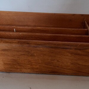 May include: A wooden desk organizer with multiple compartments. The organizer is rectangular with a light brown finish and visible wood grain. It features several dividers to separate items and has a simple, functional design. The construction includes dovetail joints.