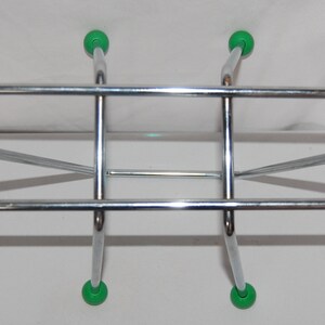 Peut inclure: Un rack en m&eacute;tal chrom&eacute; avec six pieds en plastique vert. Le rack a une forme rectangulaire avec une barre horizontale en haut et deux barres horizontales en bas.