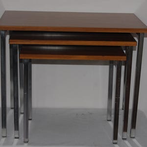 May include: A set of three nesting tables with brown wood tops and chrome legs. The tables are stacked on top of each other.