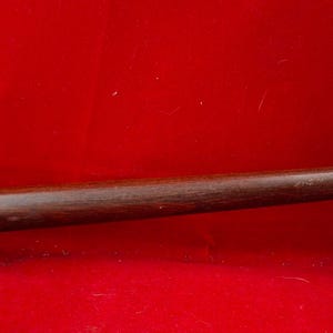 Könnte beinhalten: Ein Holzhammer mit einem dunkelbraunen Griff und einem rechteckigen Kopf. Der Kopf ist heller braun und hat eine gewölbte Oberseite. Der Hammer ist vor einem roten Hintergrund platziert.