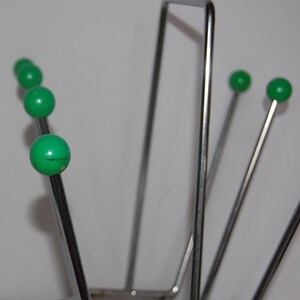 Peut inclure: Un porte-revues en chrome avec cinq extr&eacute;mit&eacute;s de boule vertes. Le porte-revues est fait de fines tiges m&eacute;talliques et a une base rectangulaire.