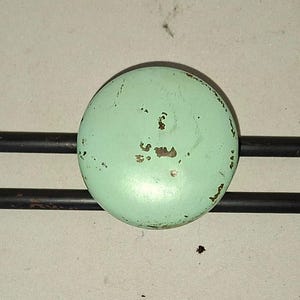 Puede incluir: Un perchero de estilo vintage con tres pomos redondos de color verde claro. Los pomos muestran signos de desgaste y están montados en una barra de metal negro. El perchero tiene un diseño minimalista con un enfoque en la funcionalidad y la estética retro.