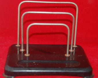 Peut inclure: Un organiseur de bureau vintage en métal noir avec trois séparateurs argentés. L'organisateur a une base rectangulaire avec des coins arrondis et de petits pieds. Les séparateurs sont incurvés en haut et fixés à la base avec de petits rivets. Le fond est de couleur rouge uni.