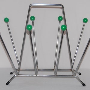 Peut inclure: Un porte-revues en chrome avec un design g&eacute;om&eacute;trique et des accents de boules en plastique vert. Le porte-revues a une base rectangulaire et un cadre triangulaire.